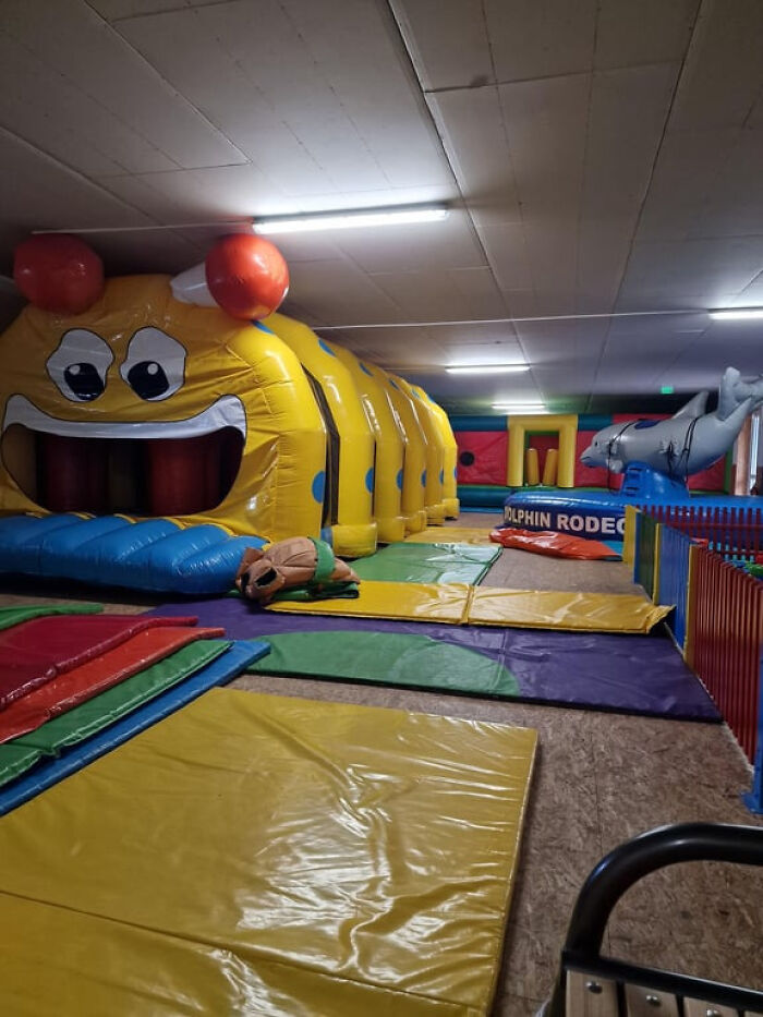 Unsettling liminal space: an empty indoor play area with a large yellow caterpillar bounce house.
