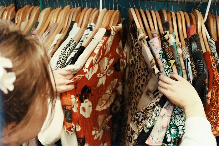 Person browsing through clothes on hangers, showcasing various patterns. An example of unusual jobs in retail.