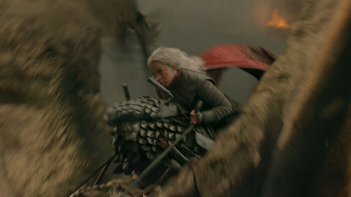 A fierce young woman with white hair rides a dragon in House Of The Dragon Season 3 during a naval clash. A fierce young woman with white hair rides a dragon in House Of The Dragon Season 3 during a naval clash.