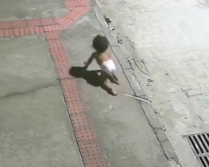 Baby crawling out at night by herself on a sidewalk, captured by surveillance footage.