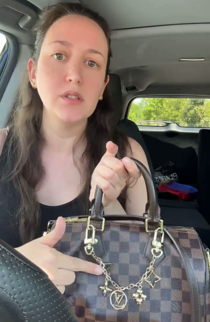 A woman holding up her Louis Vuitton bag, showing the details after a customer demands it.