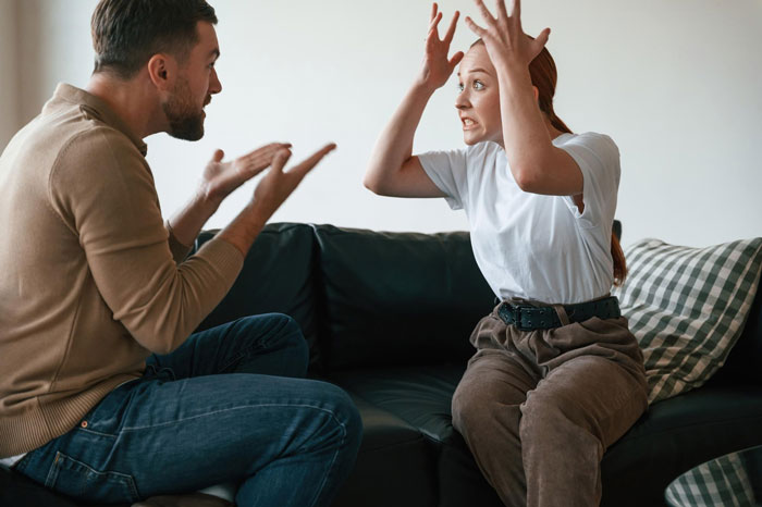 Couple having an intense argument on a couch, showing tension and frustration Couple having an intense argument on a couch, showing tension and frustration