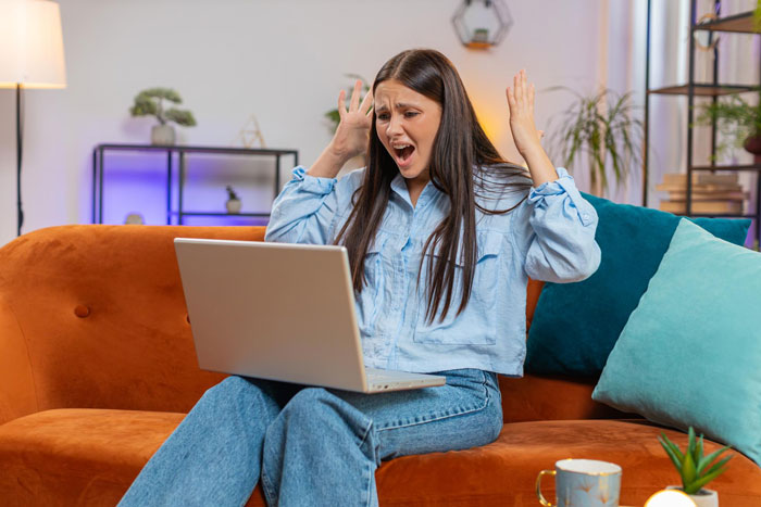 Shocked woman sitting on couch looking at laptop upset about data collection obsession Shocked woman sitting on couch looking at laptop upset about data collection obsession