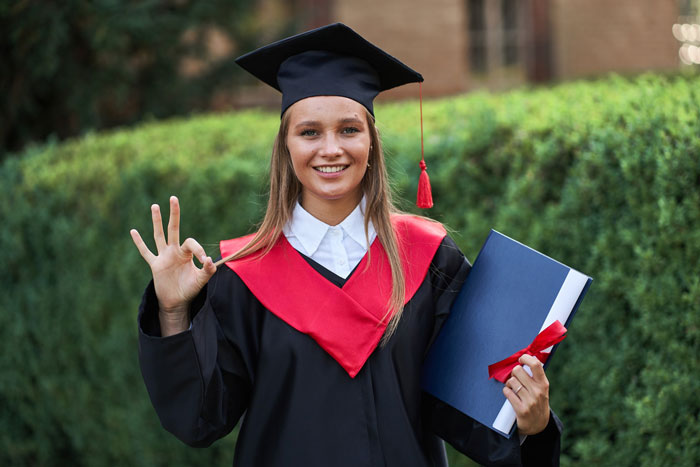 A happy graduate wearing a cap and gown, holding a diploma, smiling after escaping a toxic guy's rules.