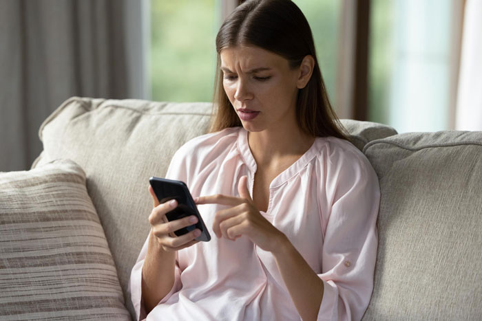 A young woman looking confused while using her phone, possibly dealing with a toxic guy and his rules.