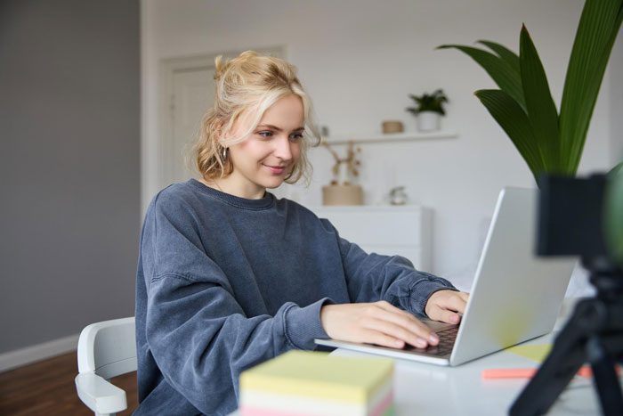 A young blonde woman smiling while working on her laptop, moving on from a toxic guy and his jealousy rules.