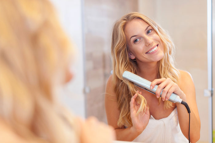 A happy woman styling her hair in a mirror after ending a toxic relationship caused by her boyfriend's jealousy