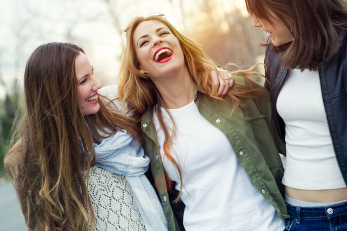 Three young women laughing and embracing, representing the joy of overcoming a toxic relationship and jealousy.
