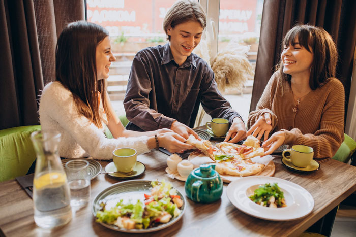 Three friends enjoy a meal at a restaurant. This image represents life after leaving a toxic guy and his rules.