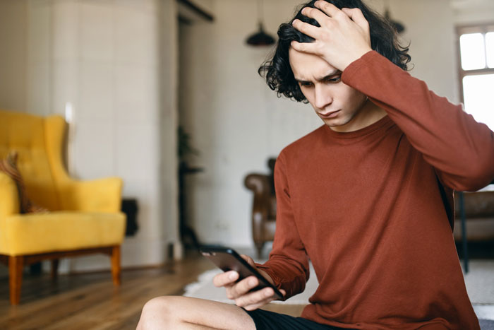 Frustrated young man looking at phone in relationship context Frustrated young man looking at phone in relationship context