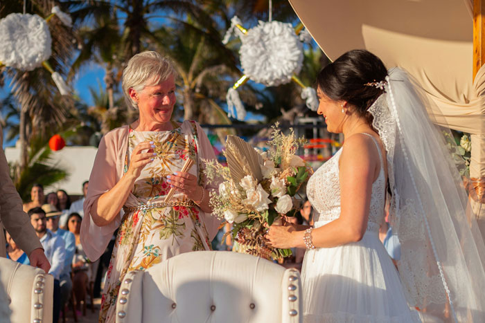 Bride and guest smiling and holding bouquet at outdoor wedding ceremony