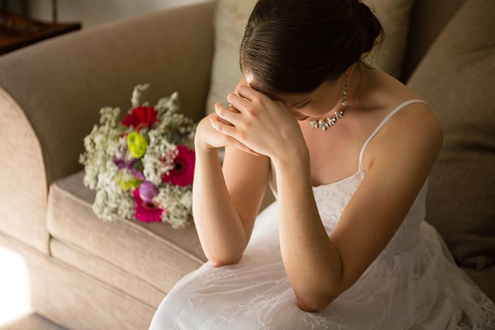 Bride sitting stressed on couch in wedding dress with bouquet Bride sitting stressed on couch in wedding dress with bouquet