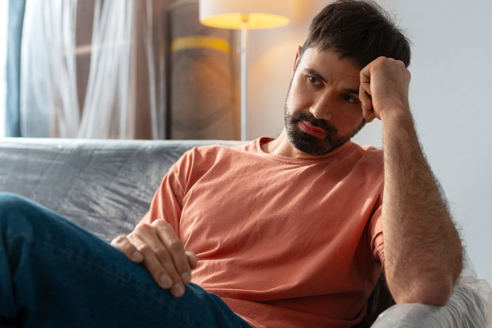 Man sitting on couch looking worried about babysitting pay feud Man sitting on couch looking worried about babysitting pay feud