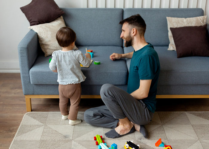Man babysitting toddler playing with toys on floor near couch Man babysitting toddler playing with toys on floor near couch