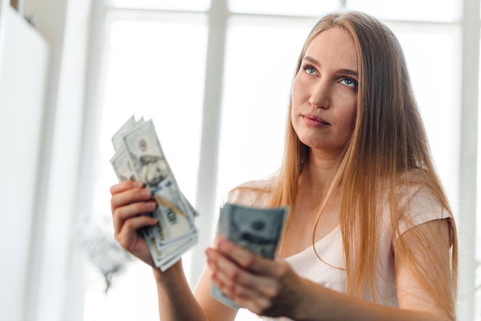 Woman holding cash with frustrated expression about babysitting payment Woman holding cash with frustrated expression about babysitting payment