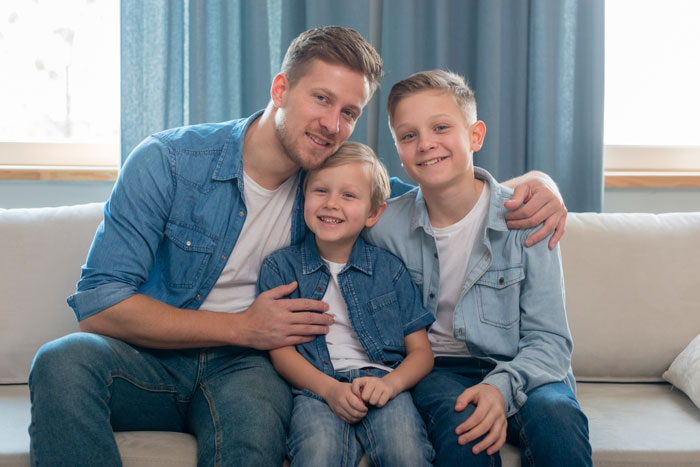 A happy father with two sons, all wearing denim shirts, posing on a sofa. Parents refuse to take bully on beach trip. A happy father with two sons, all wearing denim shirts, posing on a sofa. Parents refuse to take bully on beach trip.