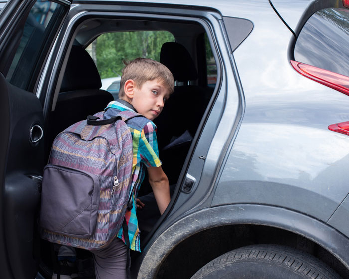 A young bully boy with a backpack looks back from inside a car, dumped on a beach trip by his mom. A young bully boy with a backpack looks back from inside a car, dumped on a beach trip by his mom.