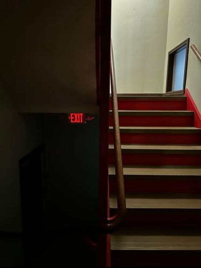 A dimly lit stairwell with a red exit sign, depicting one of many haunting liminal spaces.