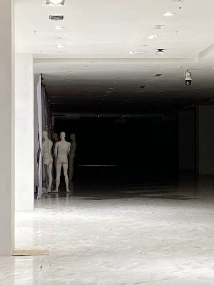 Empty retail space with mannequins peering from a dark doorway, an unsettling liminal space.
