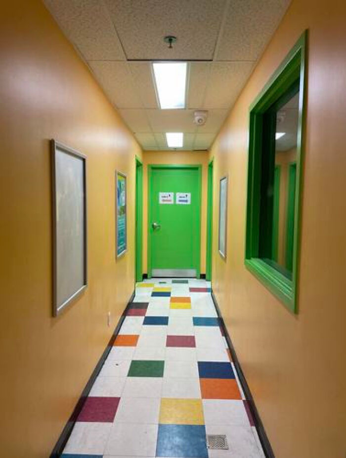 A narrow hallway with orange walls, a green door, and a multi-colored tiled floor, creating a liminal space.