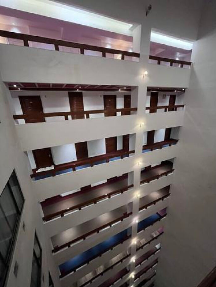 An unsettling, haunting liminal space in a multi-story building atrium looking down at identical floors.