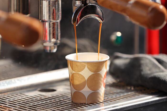Espresso pouring into paper cup from coffee machine