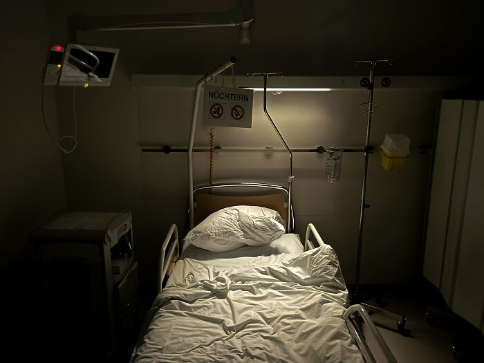 Empty hospital bed in dimly lit medical room with IV stand and monitoring equipment