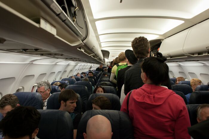Crowded airplane cabin with passengers standing and seated inside the plane interior