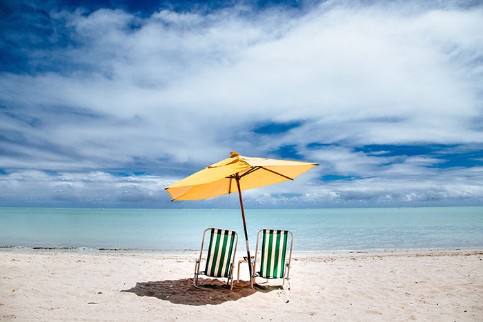 A sunny beach scene with a yellow umbrella and two empty chairs, representing the son's family vacation plans. A sunny beach scene with a yellow umbrella and two empty chairs, representing the son's family vacation plans.