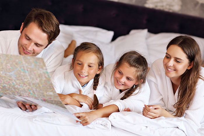 A happy family of four in bathrobes on a bed, planning their family vacation with a map. A happy family of four in bathrobes on a bed, planning their family vacation with a map.