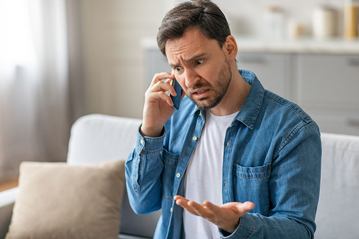 A man looking confused and upset while on a phone call, discussing parents hijacking family vacation plans. A man looking confused and upset while on a phone call, discussing parents hijacking family vacation plans.