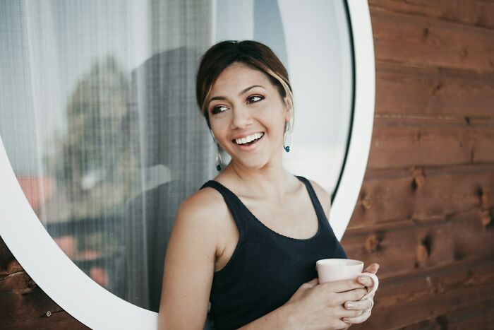Smiling woman holding cup outdoors, symbolizing confidence in impressing men