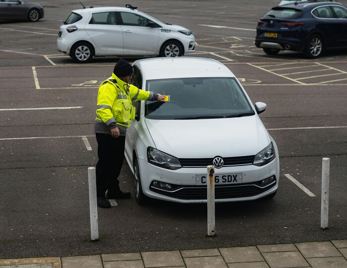 Parking enforcement officer giving a ticket to a car in a parking lot