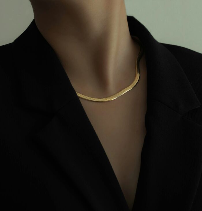 Close up of gold necklace on person wearing black blazer
