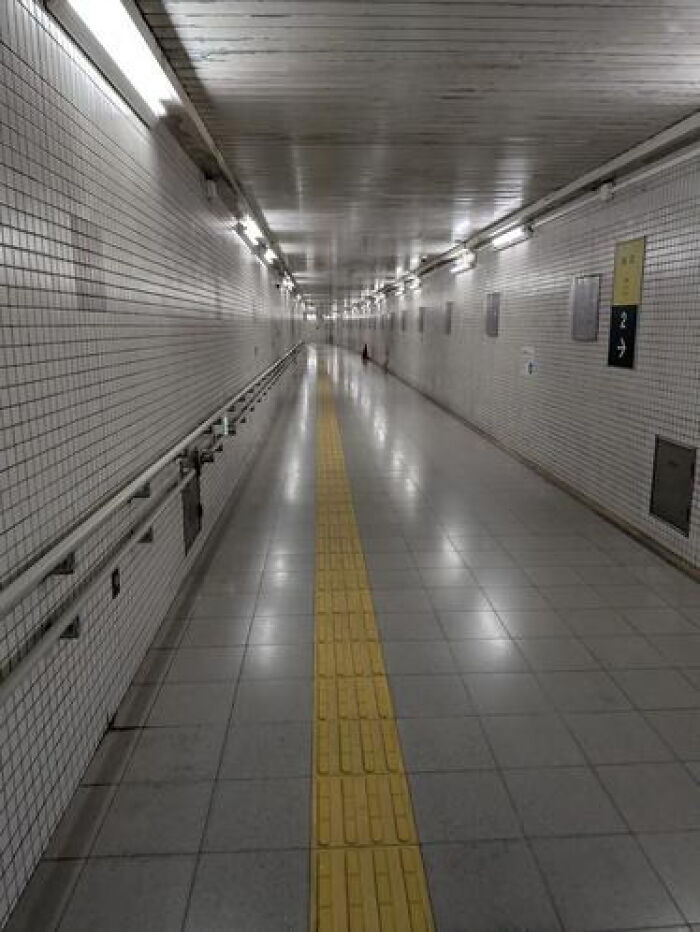 A long, deserted pedestrian tunnel with bright lights and a yellow tactile path, a haunting liminal space.