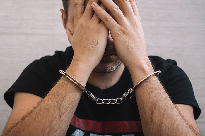 A man in handcuffs, a cheater stepdad, hides his face, reflecting the brutal revenge that led to jail. A man in handcuffs, a cheater stepdad, hides his face, reflecting the brutal revenge that led to jail.