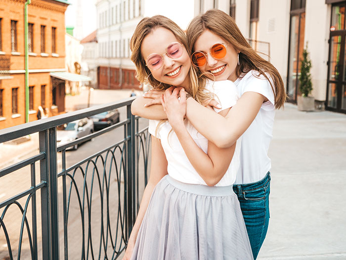 Two happy best friends, one hugging the other, symbolizing a strong friendship that could be impacted by a bridesmaid decision.