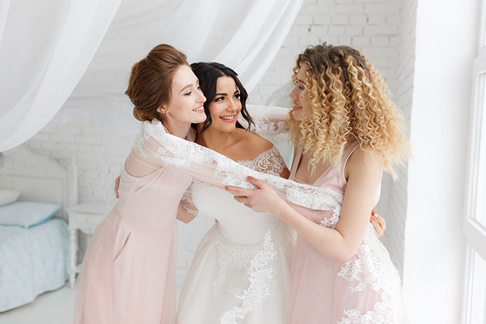 A bride and two bridesmaids embrace, highlighting the friendship that is questioned when one is not made a bridesmaid.