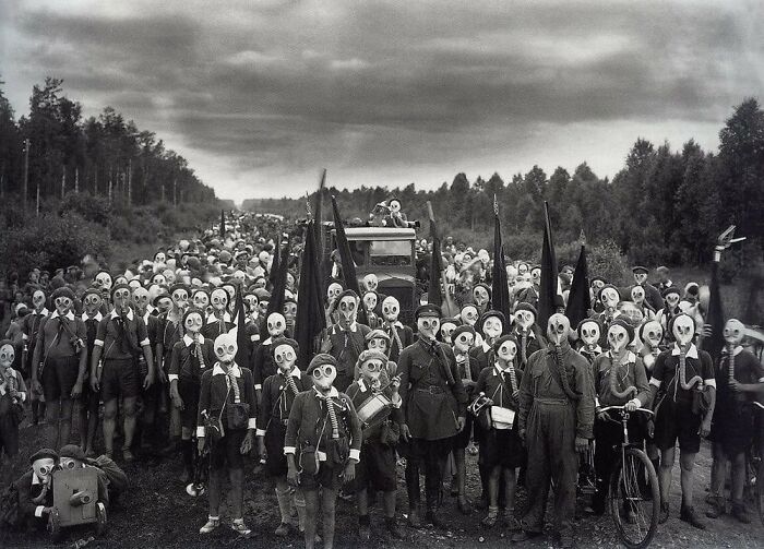 A large group of people, possibly children, wearing gas masks in a historical photo, making it impossible to explain the context.