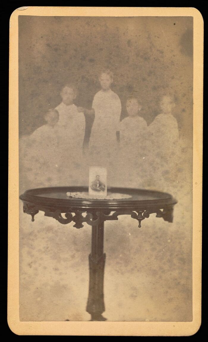 A sepia-toned historical photo shows five blurred figures behind a small table with a picture, almost impossible to explain.