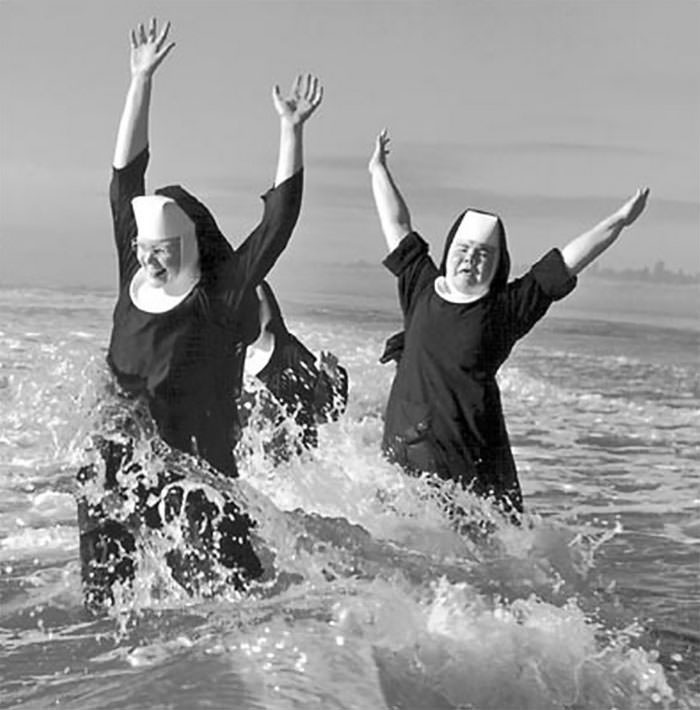 Historical photo: two nuns joyfully splashing and playing in the ocean, their habits getting wet.