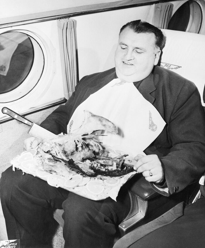 Historical photos of a large man in a suit wearing a bib, eating a huge leg of meat on an airplane with a knife.