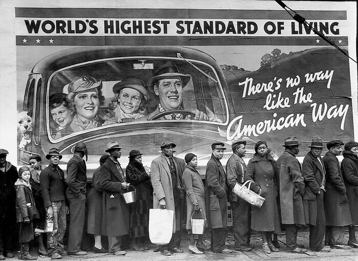 People in a breadline beneath a billboard, a historical photo feeling impossible to explain.