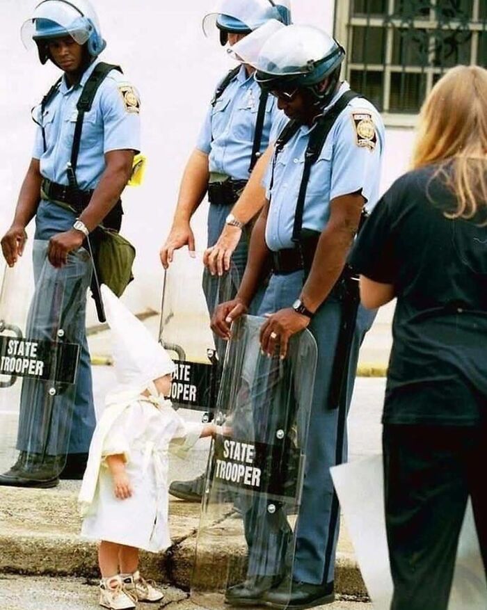 A child in a K*K outfit touches a riot shield held by a police officer, an impossible to explain historical photo.