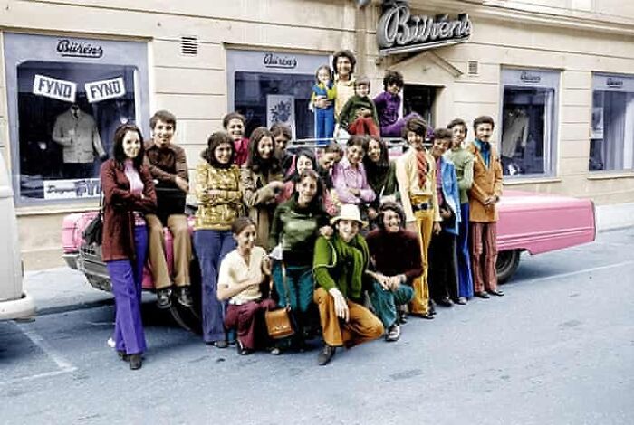 A group of people posing with a pink car outside a store, historical photos.