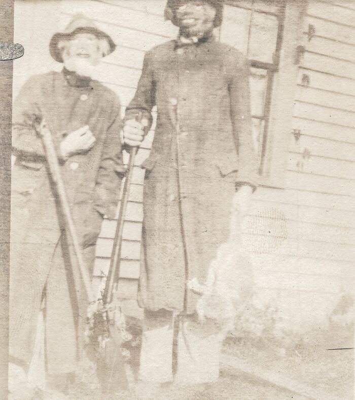 Two men in hats and coats stand with rifles in a historical photo that is impossible to explain.