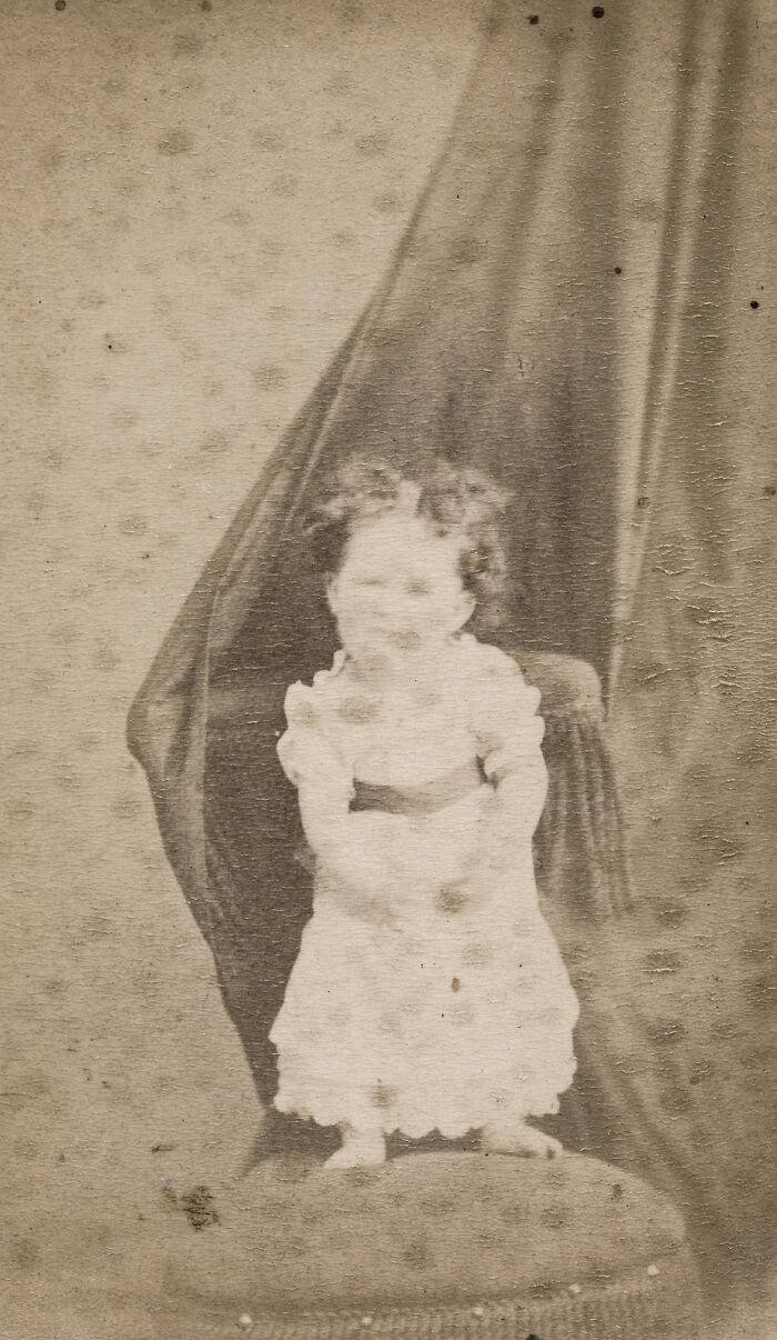 A baby with blurred features sits on a patterned cushion, one of the many historical photos.