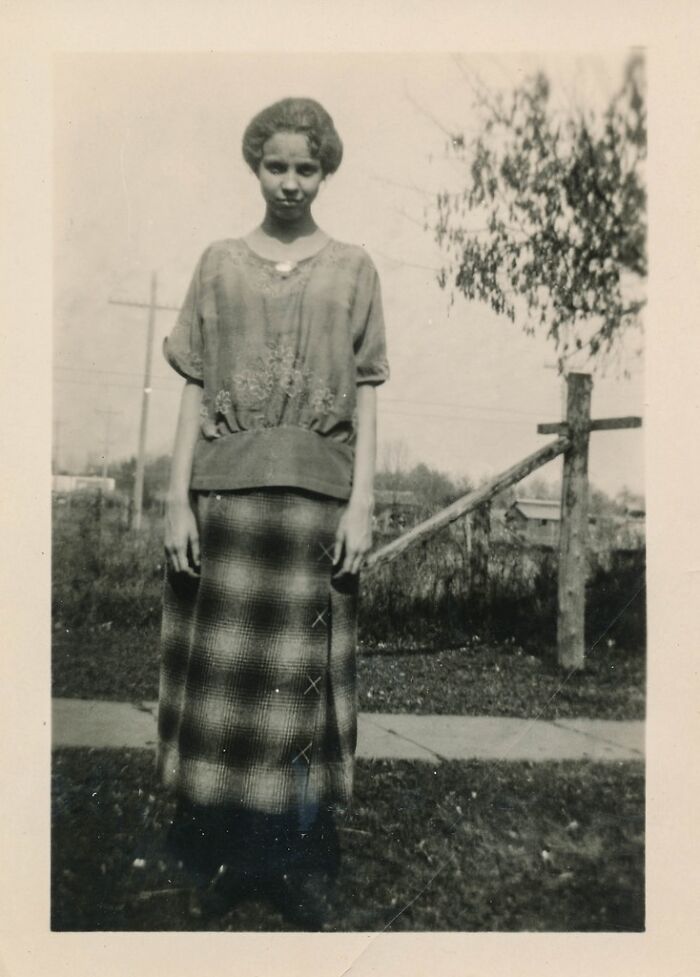 A young woman in a plaid skirt and blouse poses outdoors, one of many historical photos.