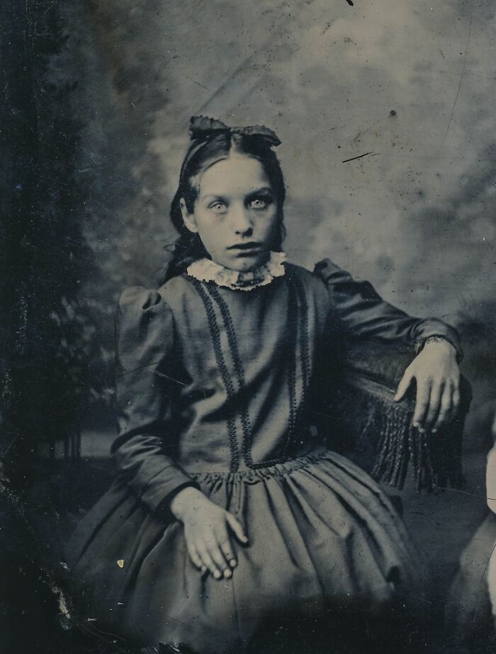 A historical photo of a young girl with piercing eyes and a bow in her hair, an unexplainable and unsettling portrait.