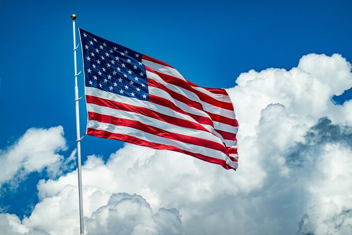 The American flag proudly waves against a bright blue sky with fluffy white clouds, representing the USA.